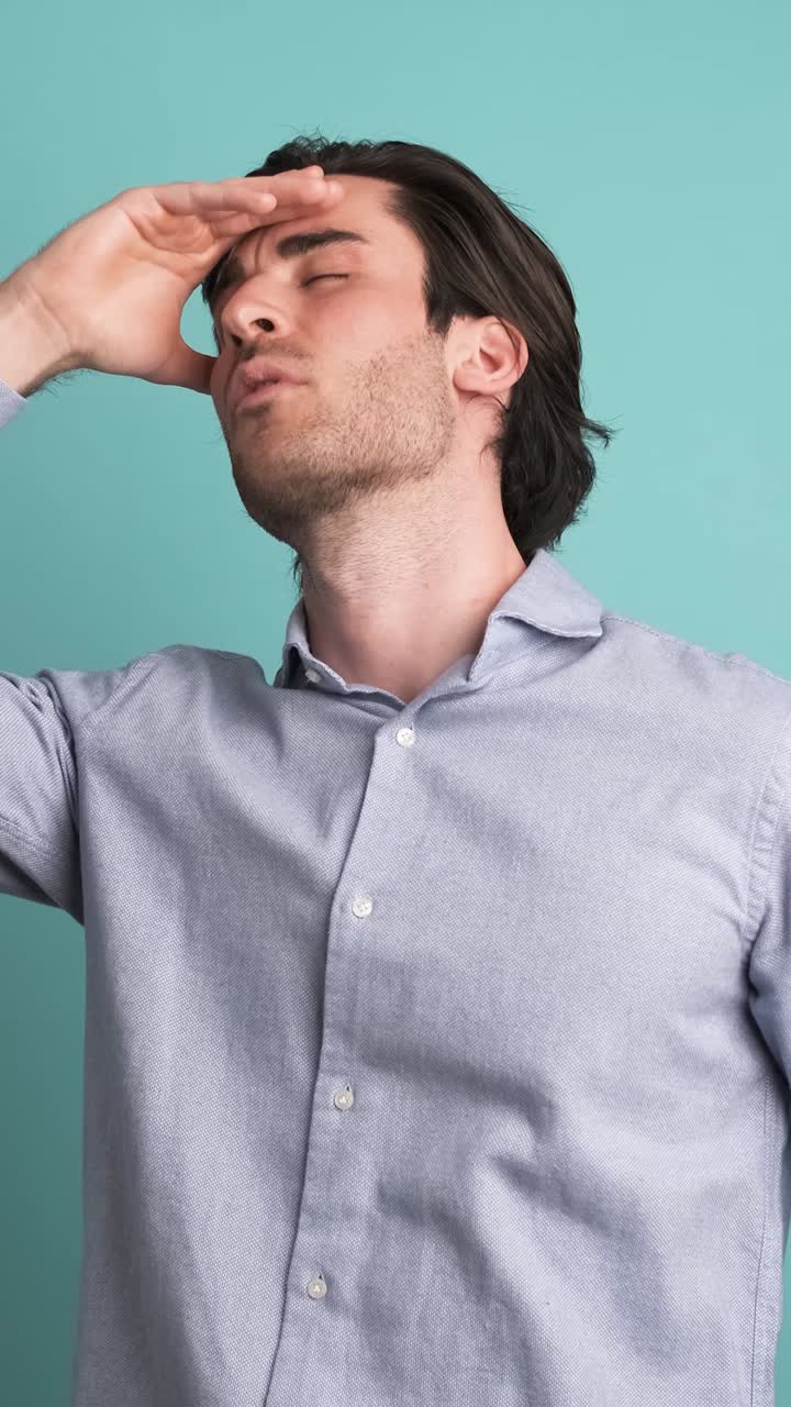 Frustrated man suffering from headache in blue studio