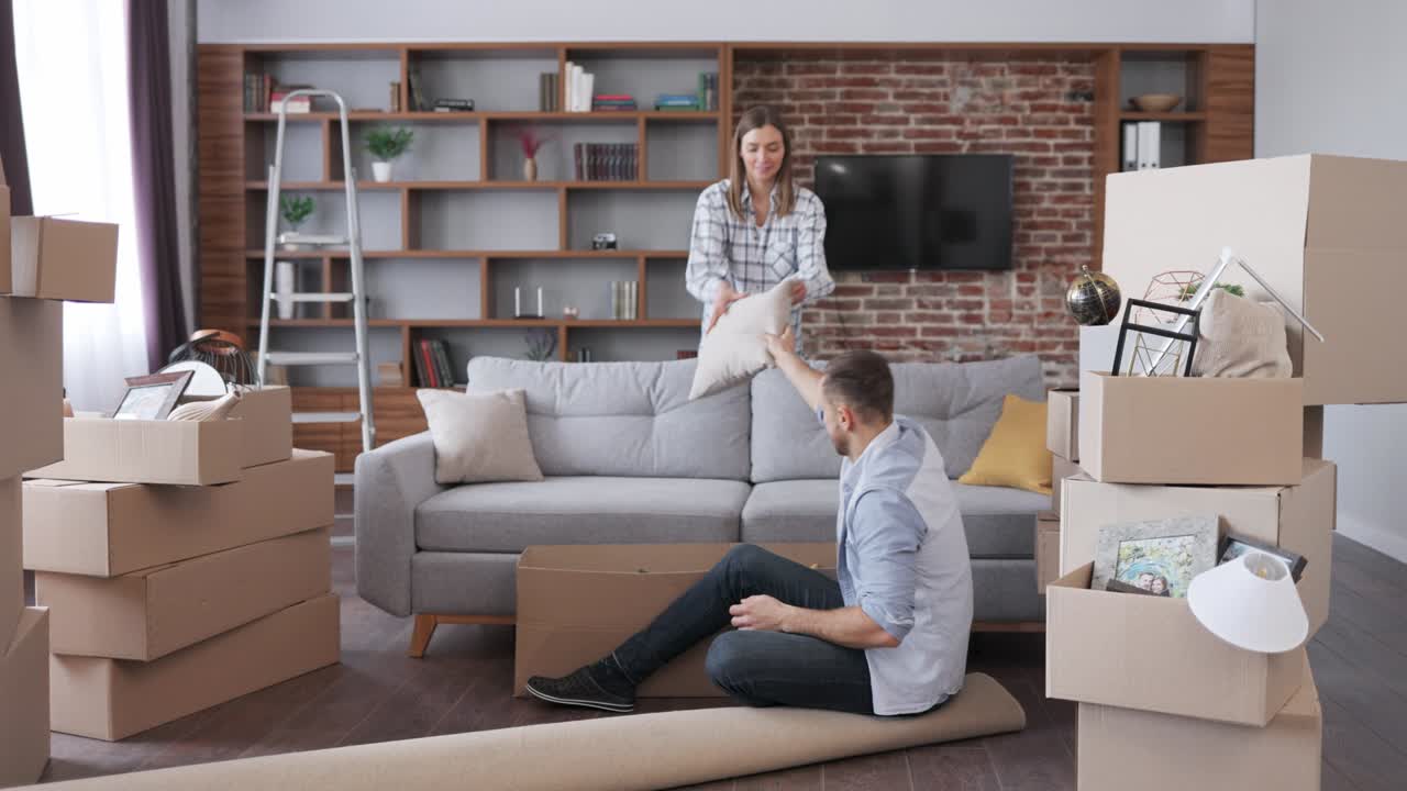 Young couple unpacking cardboard box and discussing interior design in new apartment on moving day. Happy homeowners on relocation day. Real estate and tenancy concept. Loan mortgage for young family.