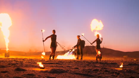 professional artists show a fire show at a summer festival on the sand in slow motion. fourth person acrobats from circus work with fire at night on the beach