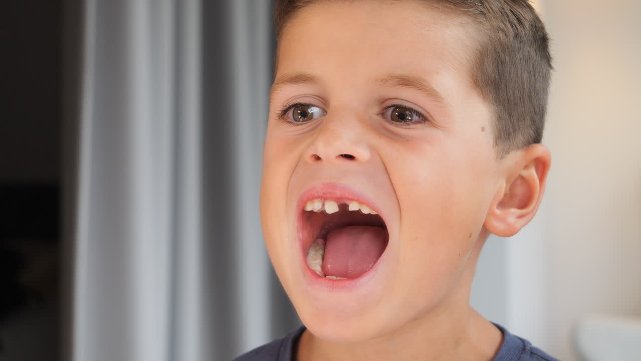 Young Caucasian Kid Tries To Pull Out Loose Milk Tooth In Front Of Mirror - Close Up