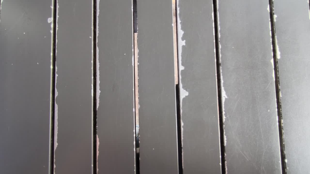 Panneaux d'aluminium gris disposés horizontalement avec des espaces réguliers. Une altération et une décoloration notables sont visibles. Les bords éraflés montrent où la peinture s'est écaillée avec le temps