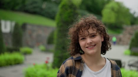 Portrait-of-a-happy-brunette-girl-with-curly-hair-who-puts-on-wireless-white-headphones-and-poses-in-the-park