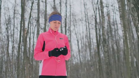 A-young-woman-on-the-morning-jog-holds-in-her-hands-a-smartphone-picks-a-music-track-for-training.-Winter-run.-Use-modern-gadgets-and-training-applications