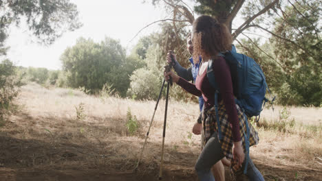 Happy-african-american-couple-hiking-with-trekking-poles-in-forest,-slow-motion