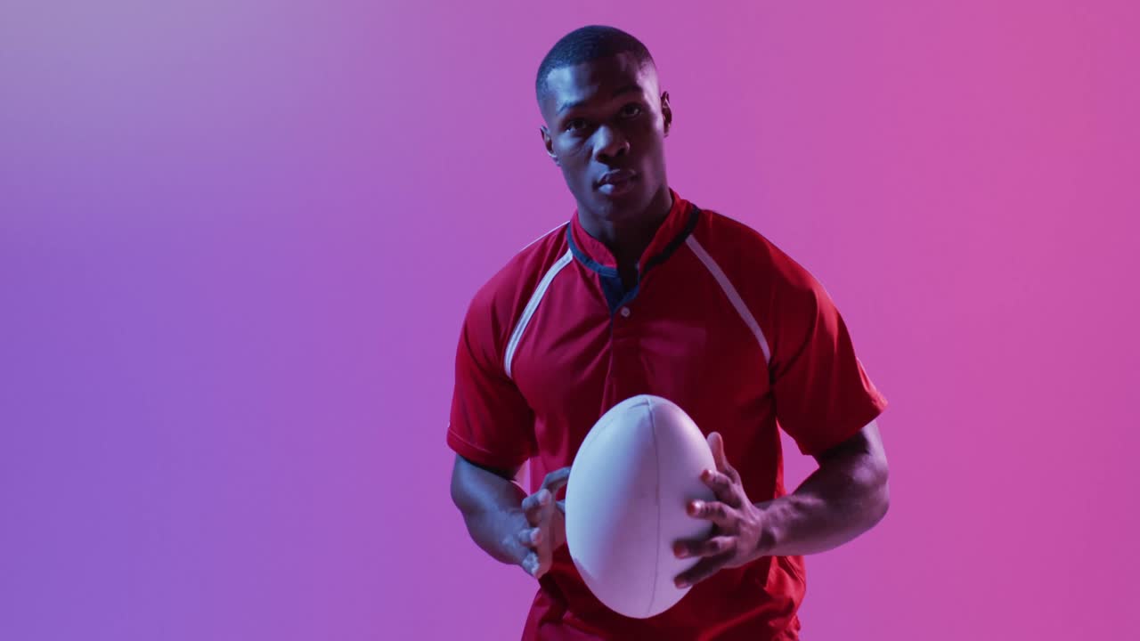 Portrait of african american male rugby player with rugby ball over pink lighting