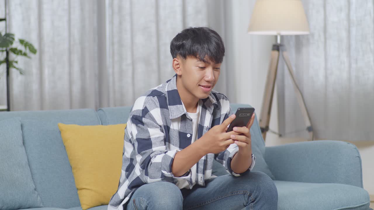 아시아 십대 소년 은 집 의 거실 의 소파 에 앉아 스마트폰 을 이용 하는 것 을 즐긴다