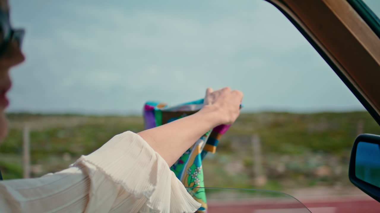 Primo piano di una donna alla guida che tiene una sciarpa fuori dal finestrino aperto dell'auto. Viaggio veloce.