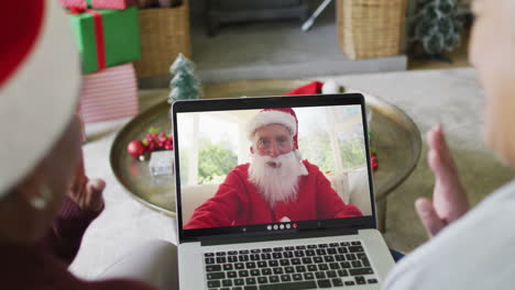 diverse senior female friends using laptop for christmas video call with happy santa on screen