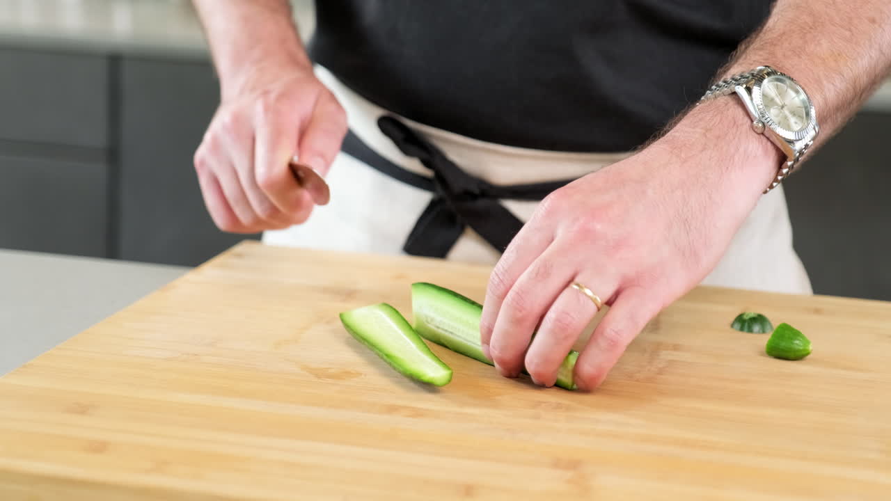 modelo masculino cortando el pepino con un cuchillo extremadamente afilado en la tabla de cortar en la cocina