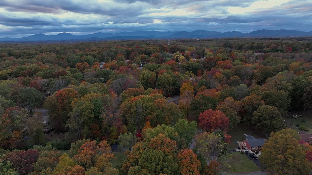 Suburb neighborhood with colorful trees in USA. Aerial wide shot. Cloudy day with silhouette of mountains in distance. Street of housing area in Virginia