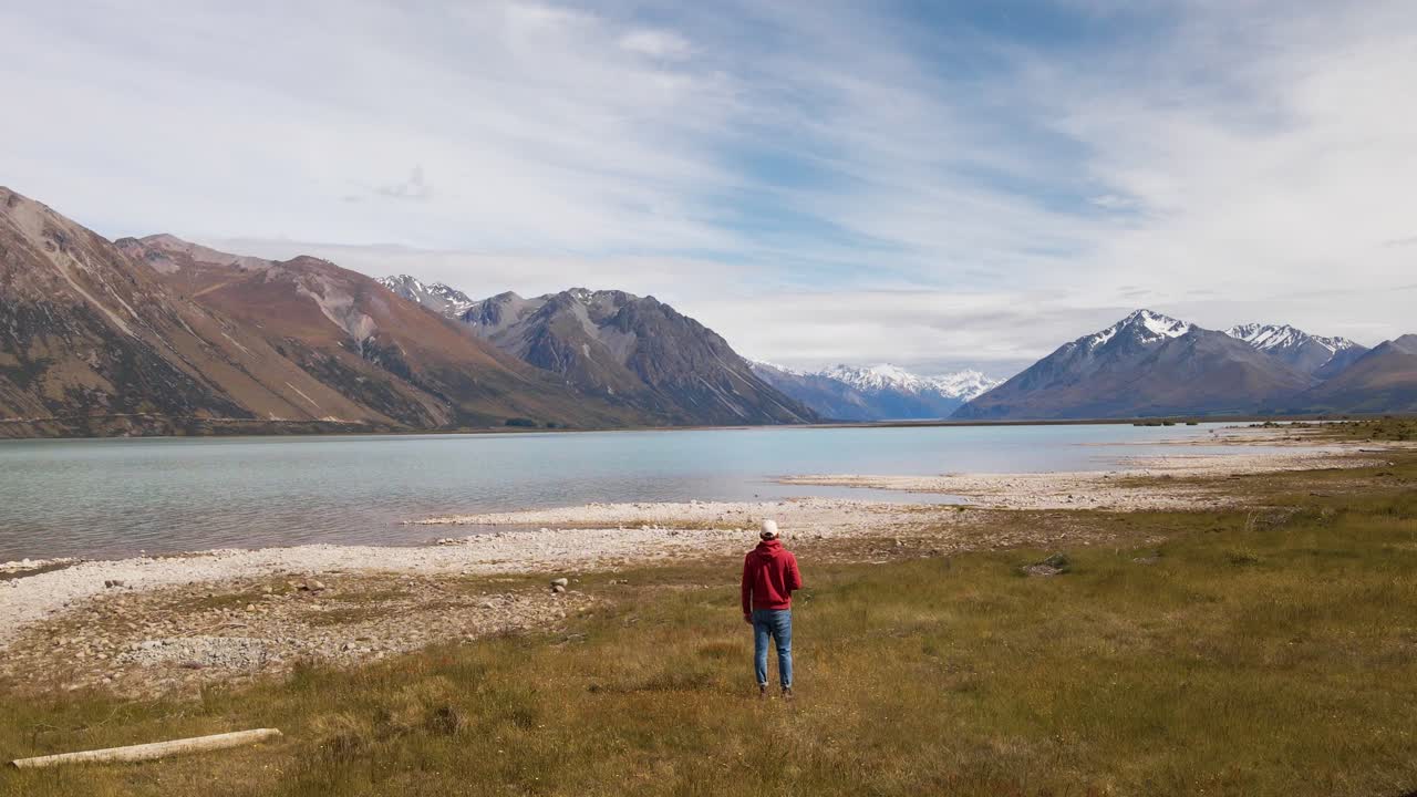 persona desde atrás caminando hacia el hermoso lago glaciar frente al pintoresco paisaje alpino