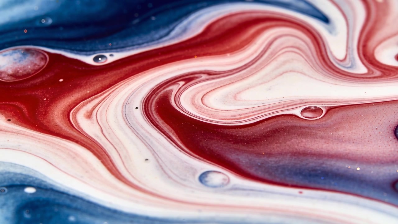 Fasce vorticose di pigmento rosso, bianco e blu che si arricciano verso l'interno su un vassoio poco profondo, seguendo lo spostamento delle goccioline.