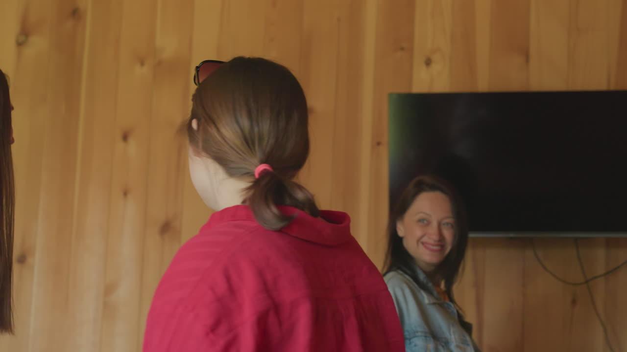 three young women exit room in cheerful mood, smiling and talking as they walk through wooden hallway, casual indoor environment with natural lighting and wooden textures