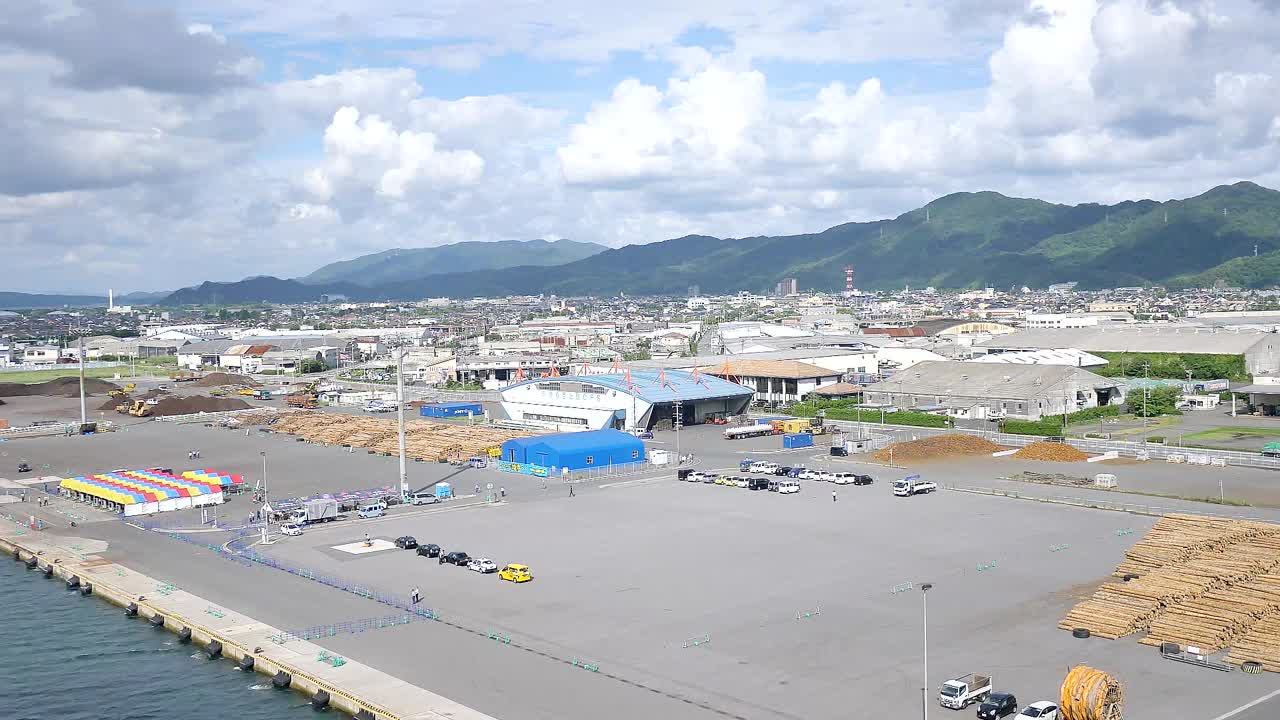 宮崎県油津港にクルーズ船が近づき、穏やかな海、沿岸の丘陵地帯、港のドッキング施設が見えてきます。