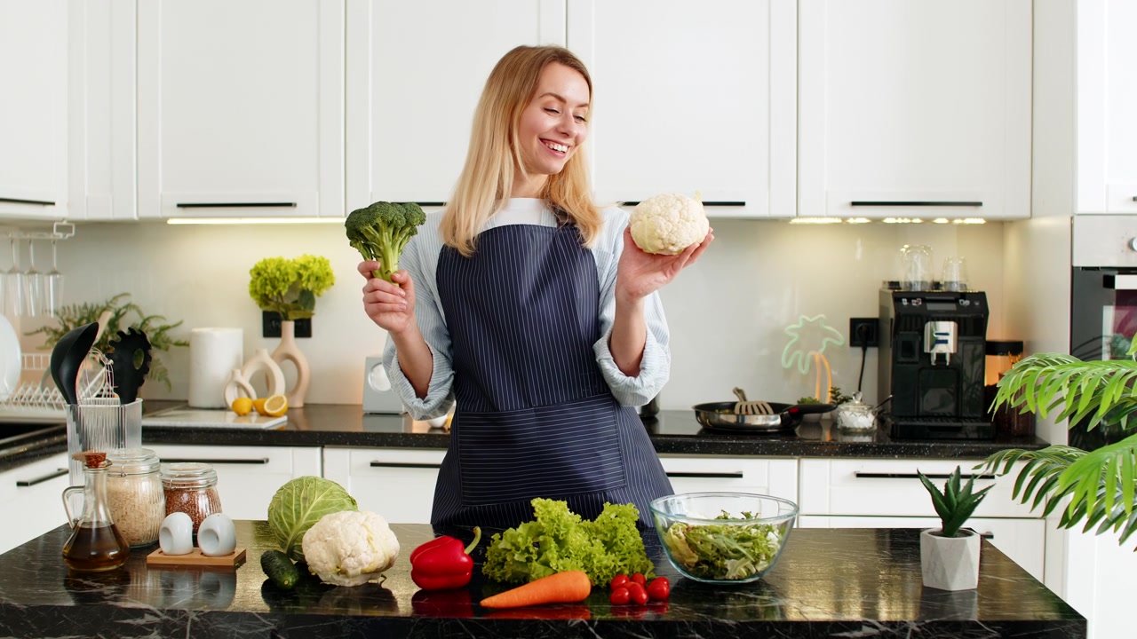 Giovane donna che mostra broccoli e cavolfiori in cucina mentre promuove l'acquisto di alimenti salutari per la dieta chetogenica
