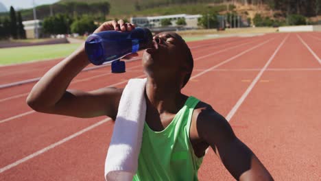 Disabled-mixed-race-man-with-prosthetic-legs-sitting-on-a-race-track-and-drinking-water