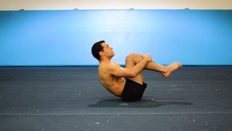 a-static-shot-of-a-guy-in-a-gymnastics-gym-doing-ab-workout-with-leg-raises-shirtless-from-a-side-front-view