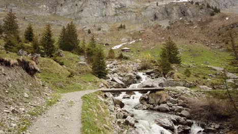 hiking trail crossing river via little bridge in the swiss alps