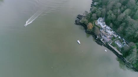 Aerial-of-the-Dartmouth-estuary-west-side-coastline-tracking-towards-the-mouth-of-the-river-as-a-speed-boat-heads-to-port-creating-a-fine-bow-wave