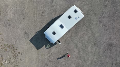 Top-down-drone-shot-of-a-man-walking-to-his-camper-van,-parked-on-a-dirt-road