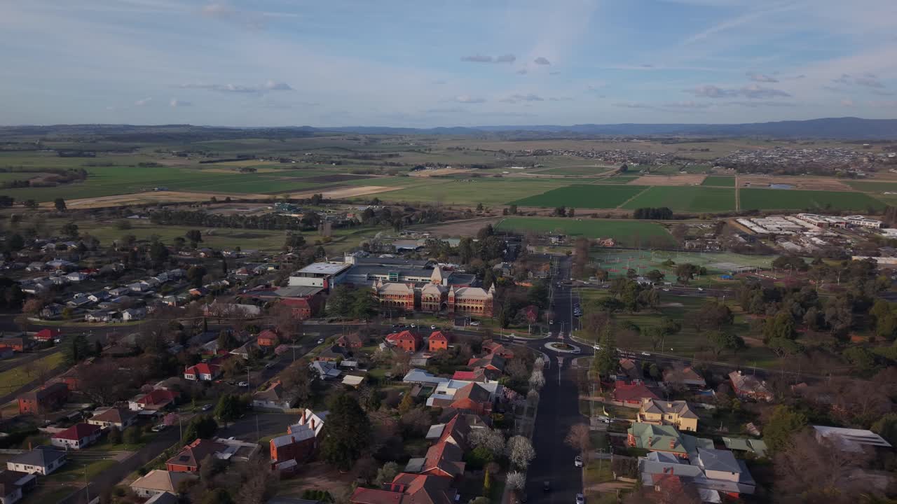 Drone orbit over green lawns and hospital buildings as sunset warms Bathurst horizon, NSW Australia, open fields backdrop