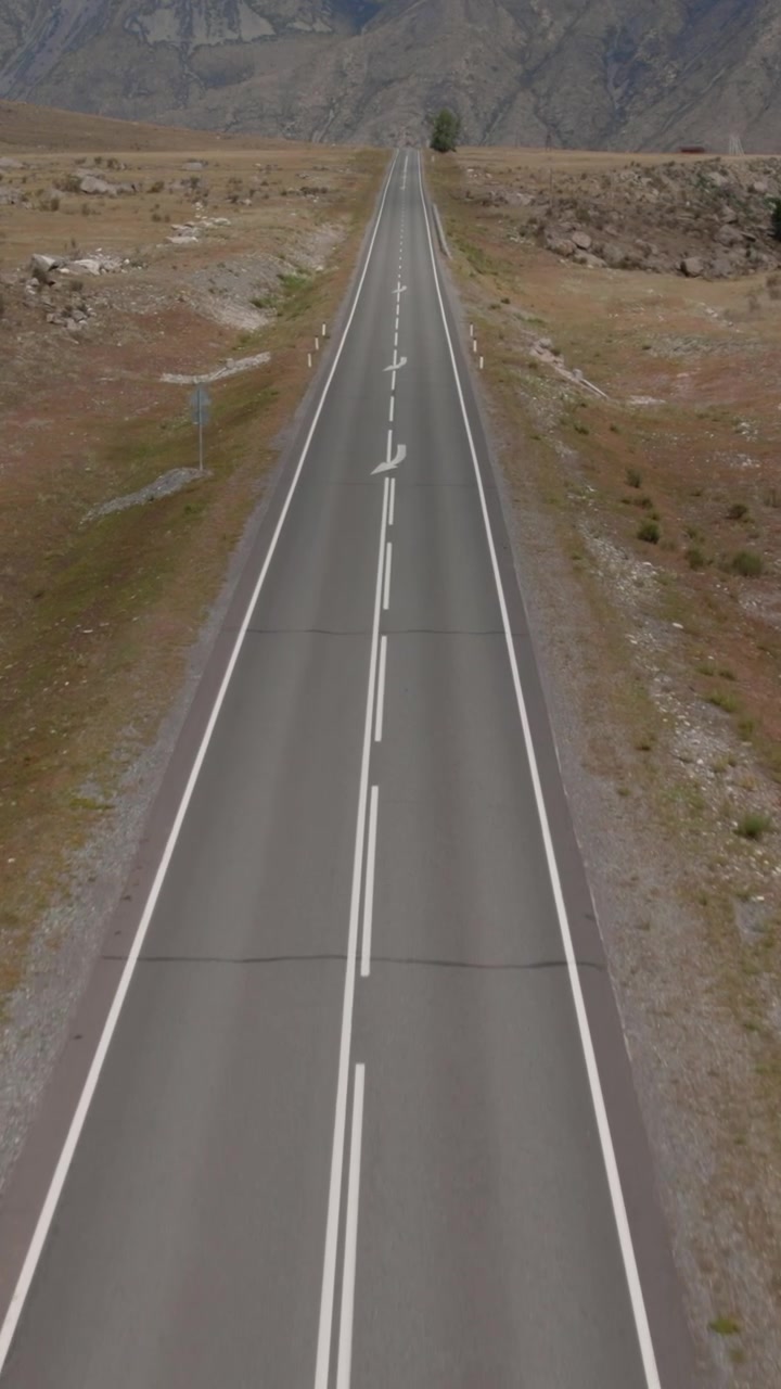 Vista drone di una lunga strada asfaltata dritta e vuota con segnaletica orizzontale che attraversa un paesaggio di valle di montagna arida sulla Chuysky Trakt, Repubblica dell'Altai, Russia.