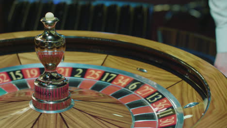 Roulette-wheel-and-croupier-hand-with-white-ball-in-casino.-People-gamble