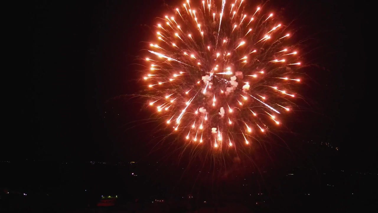 Riprese aeree con drone di fuochi d'artificio che illuminano un villaggio italiano durante una festa tradizionale locale di notte. Atmosfera festosa, pirotecnici colorati ed edifici illuminati