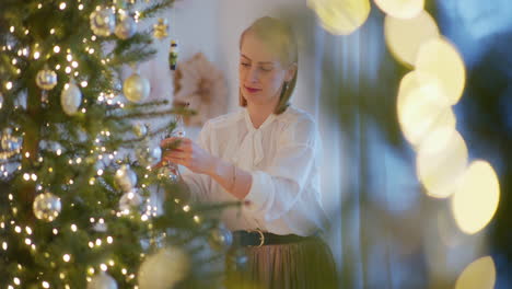 una mujer elegante y sonriente pone adornos de navidad en el árbol de navidad.