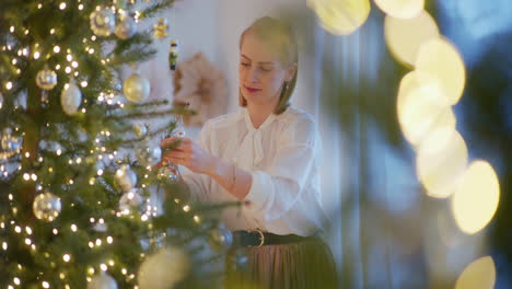 smiling elegant woman puts christmas bauble on christmas tree