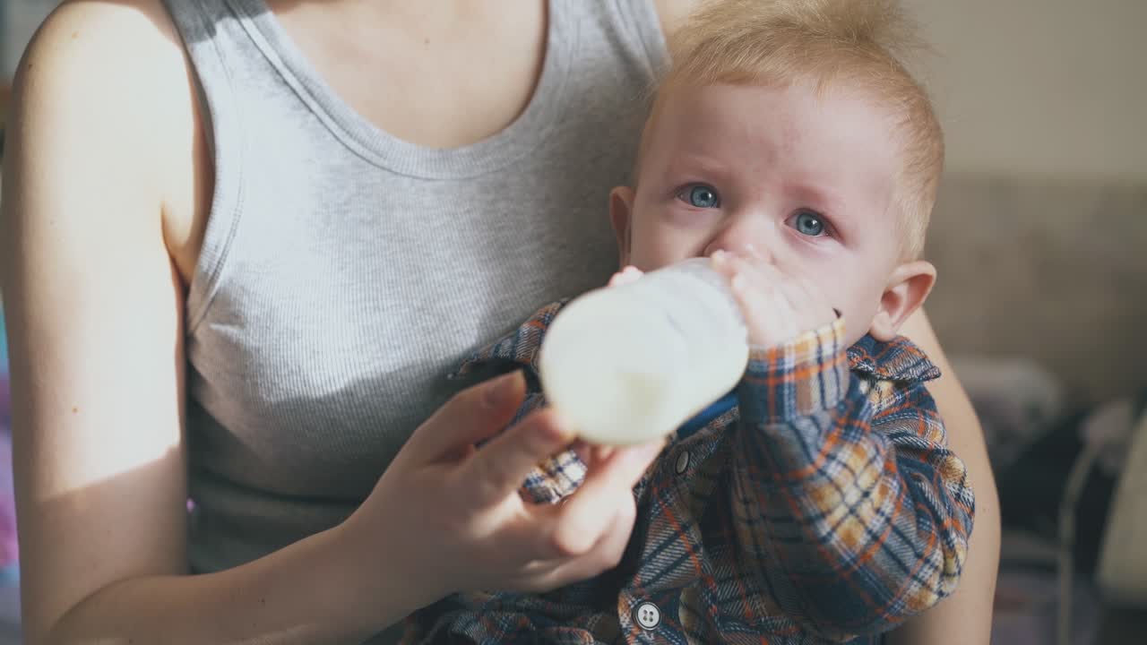 mamá alimenta a un bebé adorable de la botella en un primer plano de la habitación