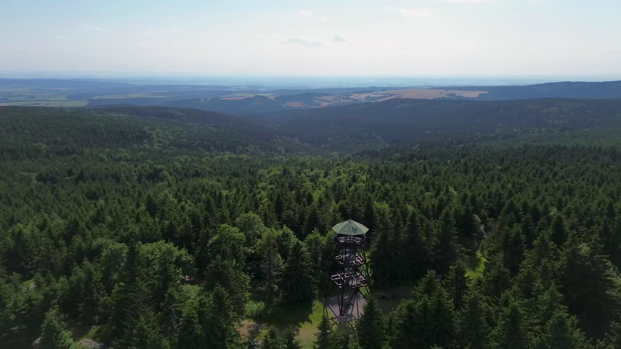 Drone view as it flies over the trees and rotates in a circle around the lookout tower on the mountains with the valley in the background