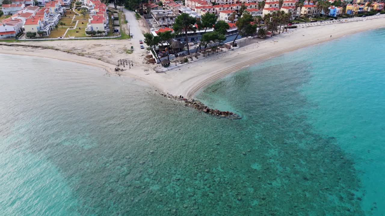 Halkidiki, Yunanistan'daki Pefkohori plajının kristal berraklığında mavi deniz suyunu gösteren havadan drone görüntüsü.