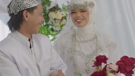 young asian newlyweds holding hands at an indonesian traditional wedding party