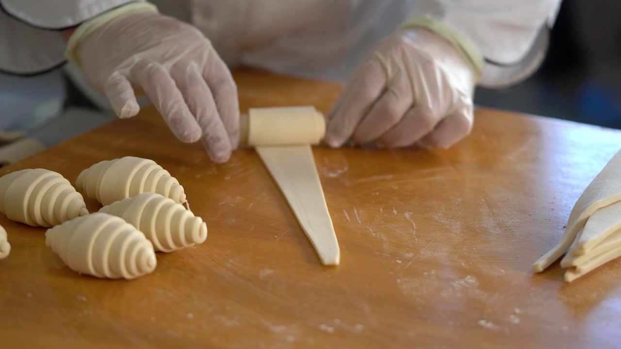 un chef de pastelería francés enrolla la masa de croissant en la mesa