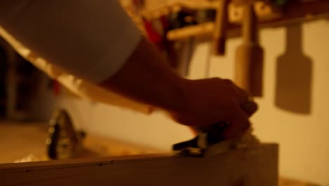 person sanding manually a piece of wood inside a workshop at sunset time