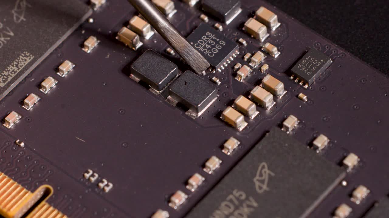 Metal tool precisely indicates microchip component on circuit board under controlled studio lighting, macro view