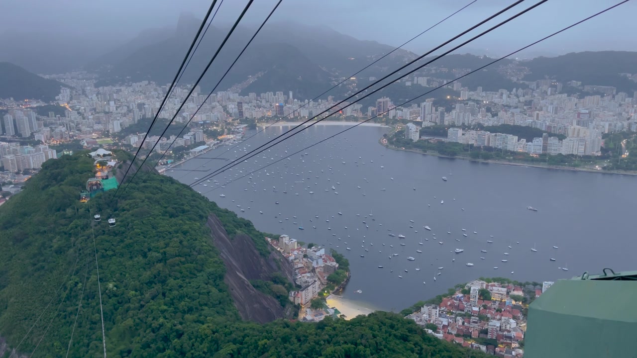 Brezilya, Rio de Janeiro'da, mavi saatte Kesmeşeker Dağı'na çıkan teleferikten havadan görünüm; teknelerle Botafogo Koyu'na, yoğun şehir manzarasına ve sisli tepelere bakıyor.