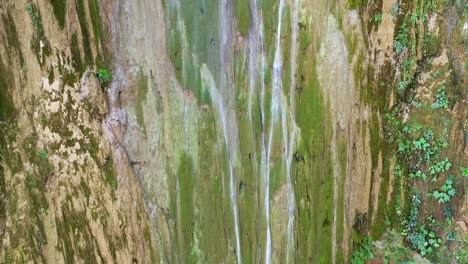 Tiro-De-Dron-Ascendente-A-Lo-Largo-De-Una-Pared-Rocosa-Cubierta-De-Musgo-Con-Una-Cascada-Que-Se-Estrella-Durante-El-Día-Soleado---Salto-Del-Limon,-Samana,-República-Dominicana