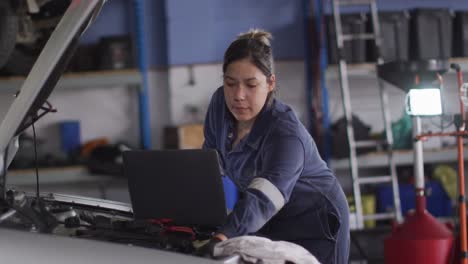 Mecánica-Femenina-Usando-Una-Computadora-Portátil-E-Inspeccionando-El-Automóvil-En-Una-Estación-De-Servicio-De-Automóviles