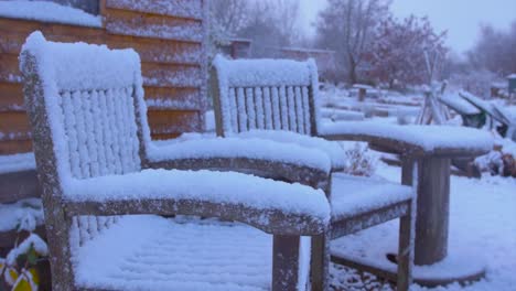 two chairs covered in snow as it continues to fall