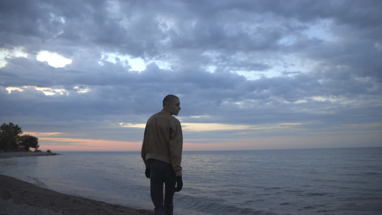 un joven caminando por la orilla mientras mira la hermosa playa - plano general