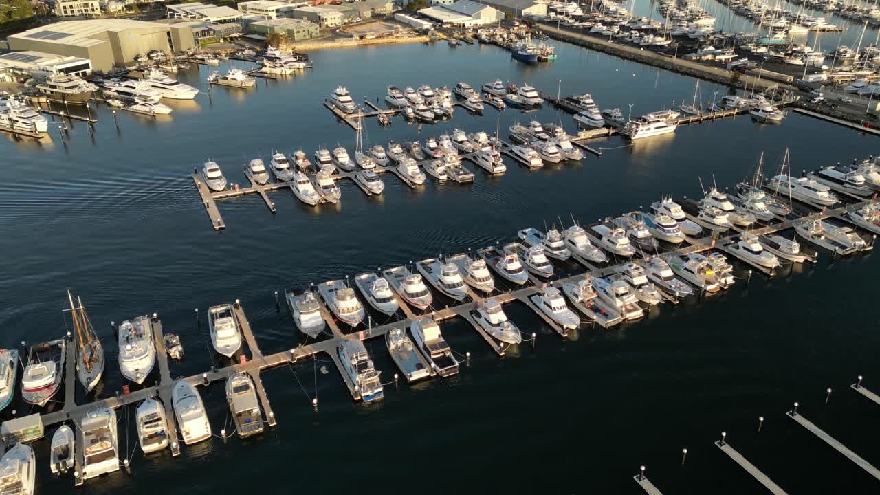 Aerial flyover luxury marina with arriving boat parking at landing pier during golden sunset - Perth City, Western Australia