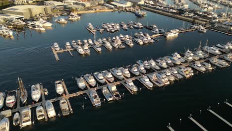 Aerial-flyover-luxury-marina-with-arriving-boat-parking-at-landing-pier-during-golden-sunset---Perth-City,-Western-Australia