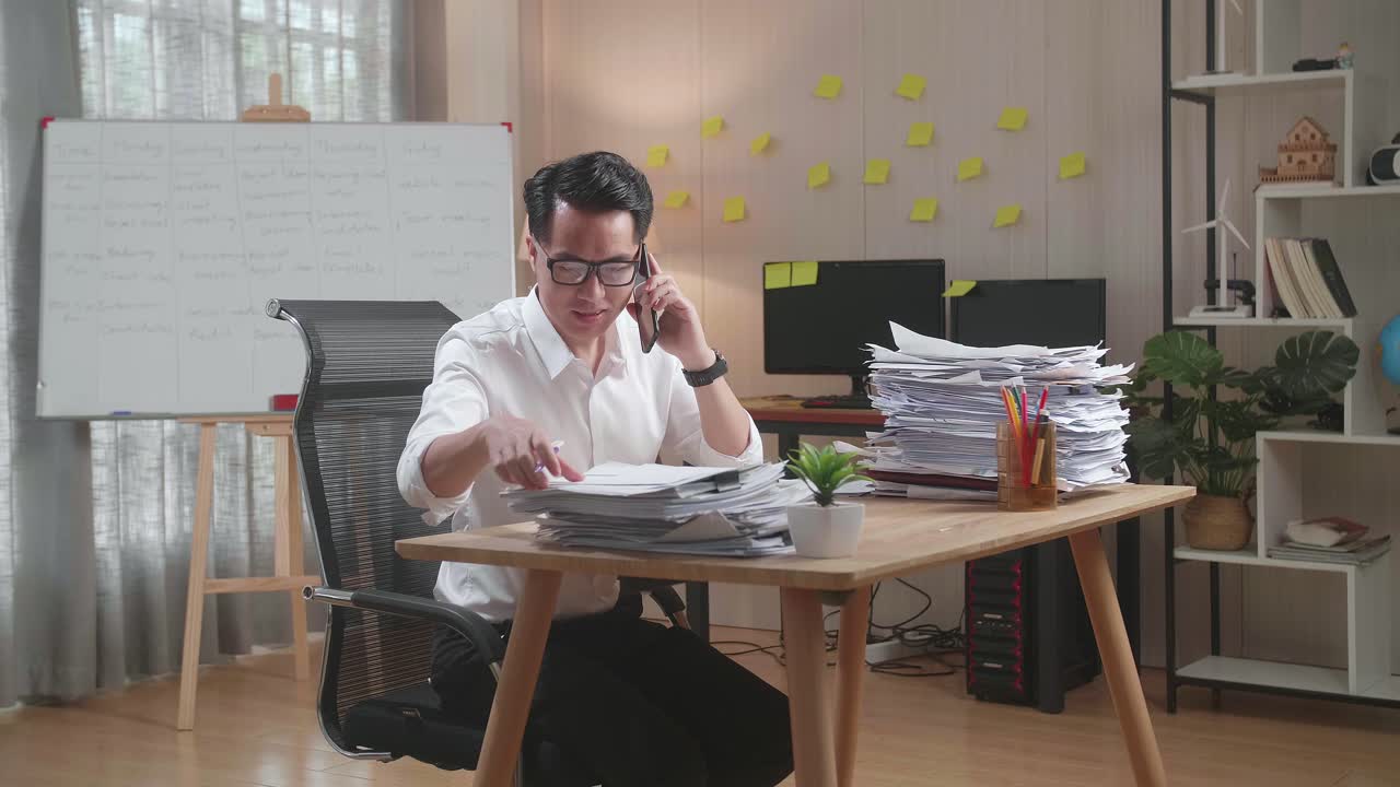 hombre trabajando en la oficina de casa con un montón de papeles y haciendo una llamada telefónica