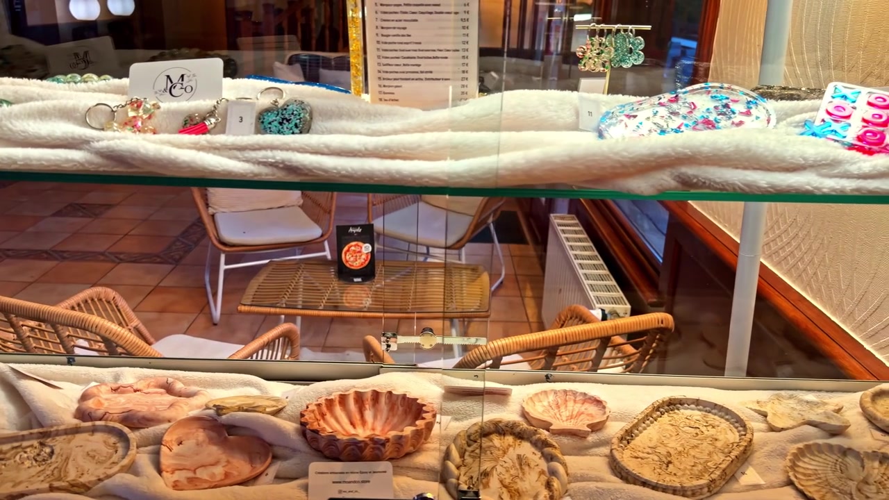 Una vetrina in vetro espone un assortimento di conchiglie e gioielli, con sedie in vimini visibili sullo sfondo. Adatto per temi di vendita al dettaglio o di interior design.