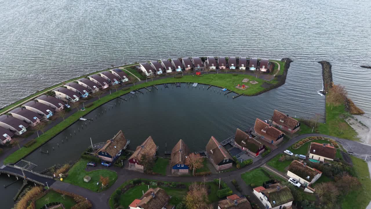 Aerial flyover dutch neighborhood houses of apartment holiday resort in Ijsselmeer, The Netherlands. Luxury similar homes in first row. Top down. Sea and bay In fall