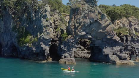 kayak al lado del arco de roca en la costa de la isla ballena moutohora, día soleado