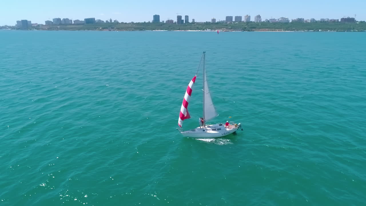 Sailboat floating on sea. Sailing yacht at sea bay. Sun seascape with sail boat on the background of the city. Small ship at open sea. Circling view.