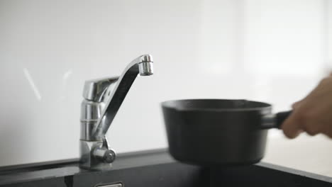 las manos masculinas llenan una pequeña olla negra con agua con un grifo plateado